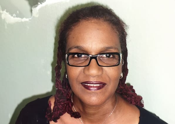 A woman with glasses and dreadlocks is smiling.