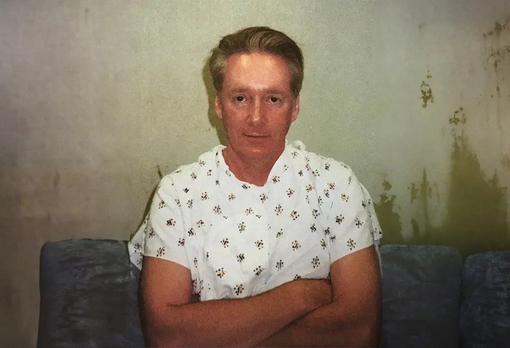 A man in white shirt sitting on couch with arms crossed.