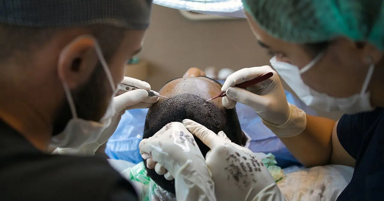 A person getting their head shaved by two doctors.